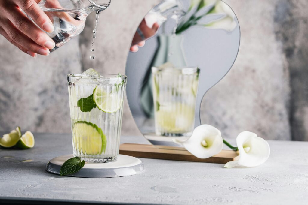 Glass of lime and mint water with a modern mirror reflection and calla lilies.